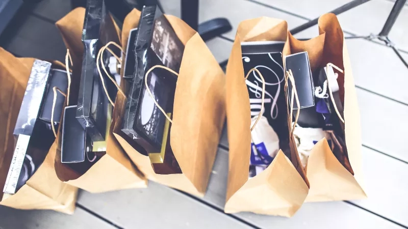 Three brown shopping bags filled with black boxes are placed on a wooden floor from above.