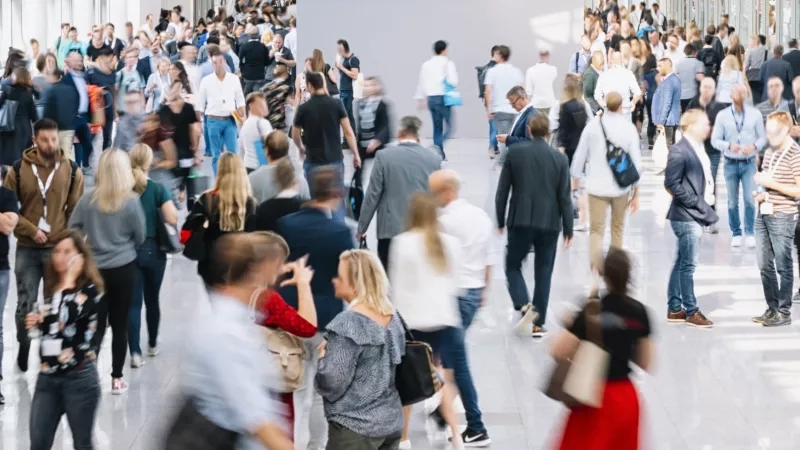Large group of people walking in a busy lobby, some blurred, others in focus.
