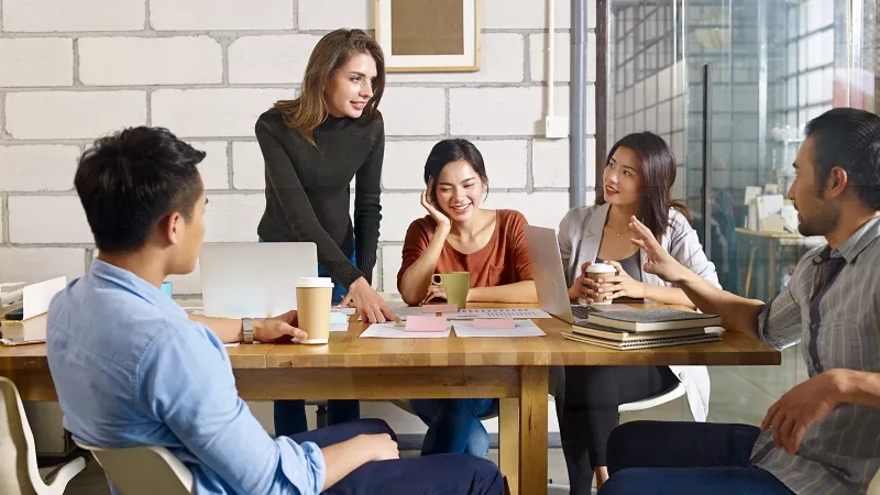 Five people are sitting in front of a desk while one person is standing and talking.