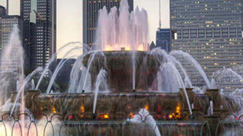 The Buckingham Fountain in Chicago, Illinois, with a city skyline backdrop and green trees in the foreground.