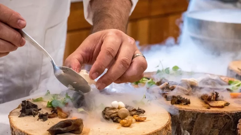A chef is preparing a vegetable dish on a tree slab.
