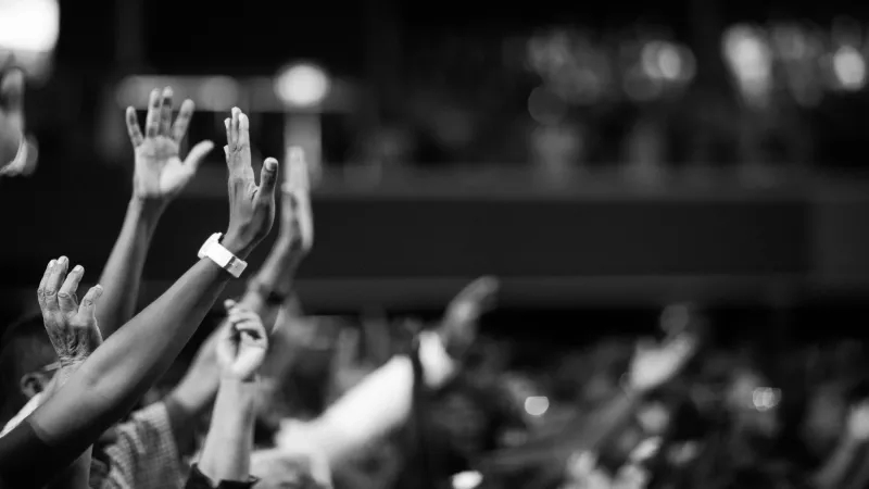 Black and white photograph of a crowd of people with their hands up in a church.