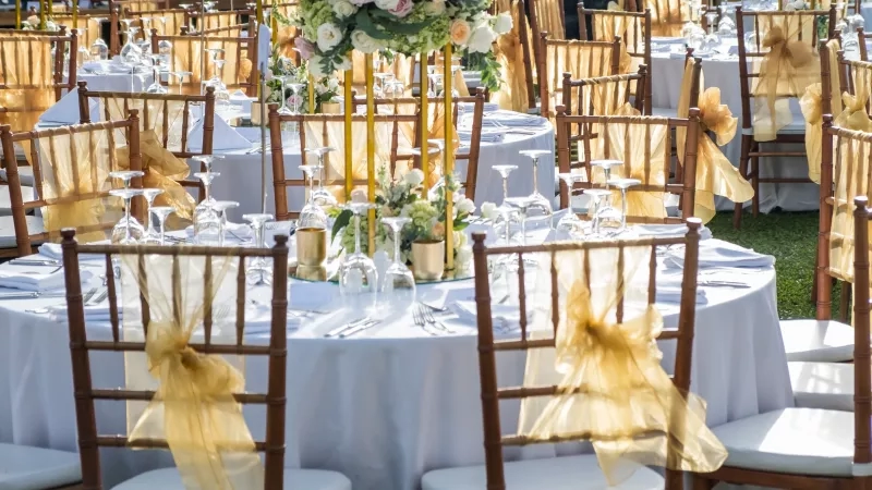 Wedding venue with round tables and white chairs decorated with yellow ribbons and flowers for a special event.