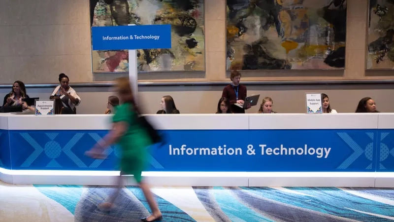 A woman is walking towards the Information & Technology counter with a laptop on it.