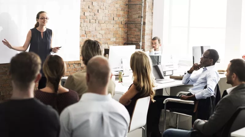 Woman in front of group of people giving a presentation in a classroom.