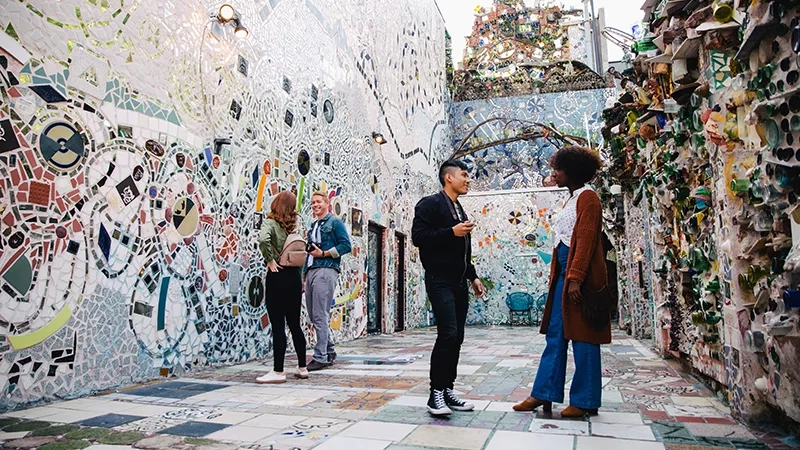 A group of people talking in the Magic Gardens, a mosaic-covered outdoor art environment in Philadelphia.