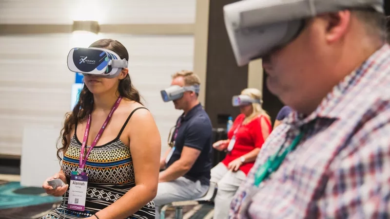A group of people are sitting in chairs and wearing virtual reality glasses inside the building.