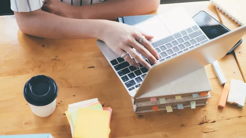 A woman is using a laptop on top of a stack of books.
