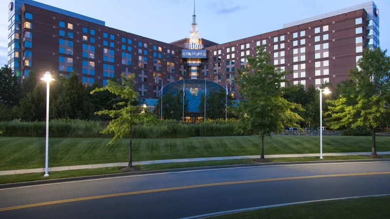 Hilton Boston Logan Airport exterior with lush greenery, tall trees, and modern architecture at dusk.