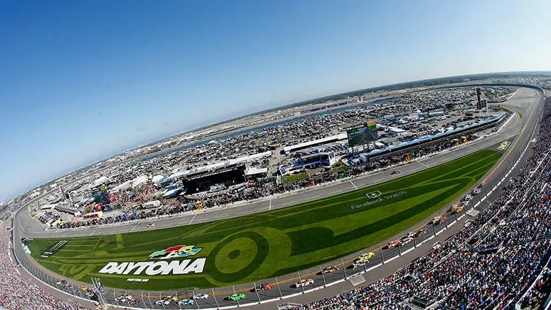 Daytona International Speedway racetrack with a crowd of people watching the cars in a race.
