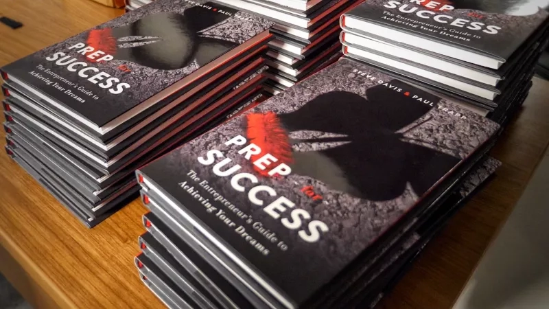Prep for Success book by Steve Davis and Paul Trapp on a wooden table in a dimly lit room.