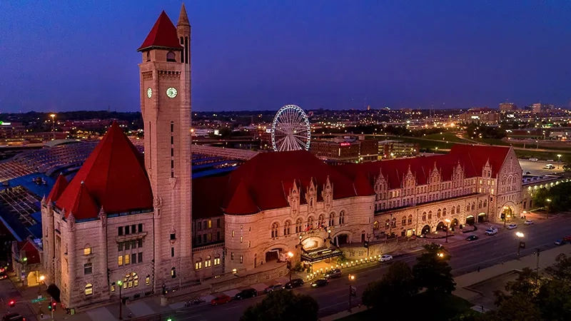 Union Station exterior at night, with a clock tower, red roof, and Ferris wheel in the background.