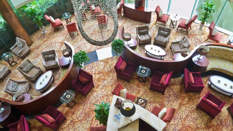 Top-angle view of a hotel lobby with couches, potted plants, and glass windows during the day.