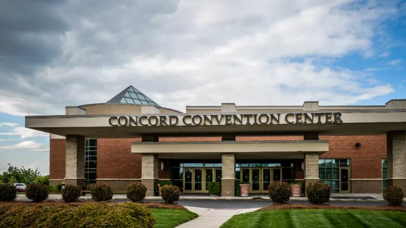 Front view of Concord Convention Center with a brick facade, glass doors, and lush landscaping under a cloudy sky.