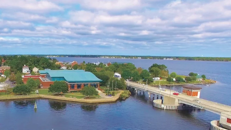 An aerial view of a bridge and a building on a waterfront with a cloudy sky.
