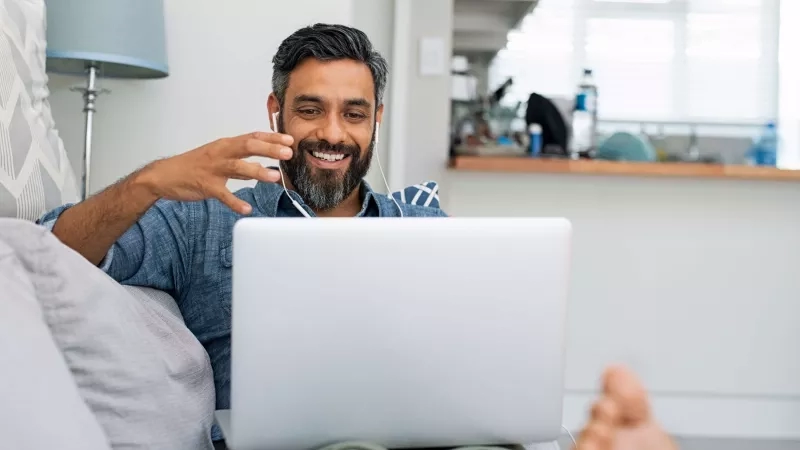 Man on couch at home video calling on laptop