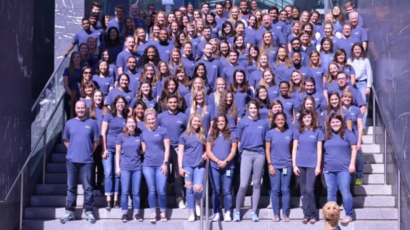 A large group of people are wearing the same blue shirt and standing on a building's stairs.