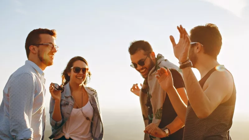 A group of friends are standing together on a sunny day, smiling and laughing with each other.