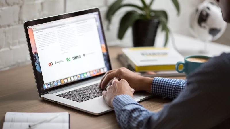 Person typing on laptop in office with notebook, pen, coffee, and globe on desk.