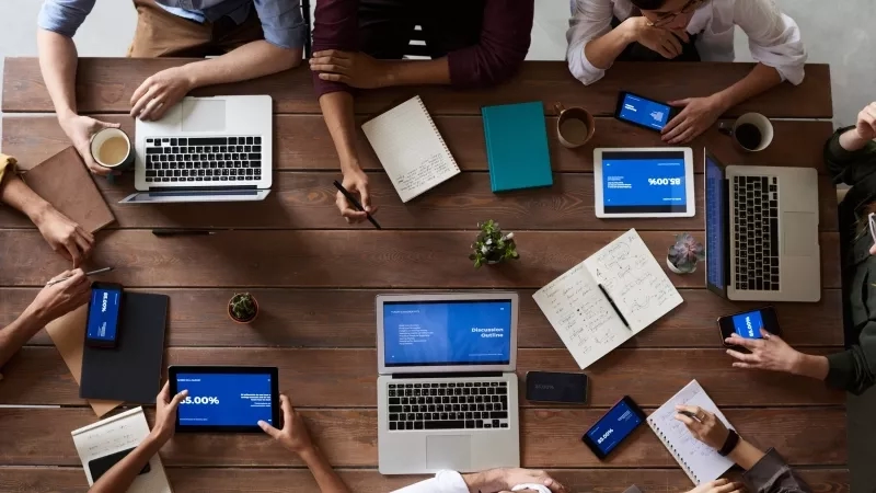 People at a table with laptops, tablets, and phones planning for the future.