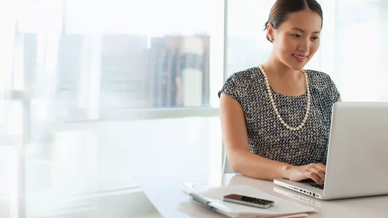 A woman sitting at a table with a laptop in an office with a view of the city.