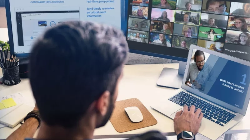 A man working on a laptop with a webinar going on the screen in front of him.