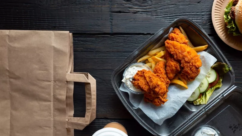 Chicken nuggets, fries, and salad in a take-out container with a bag and coffee on the side.