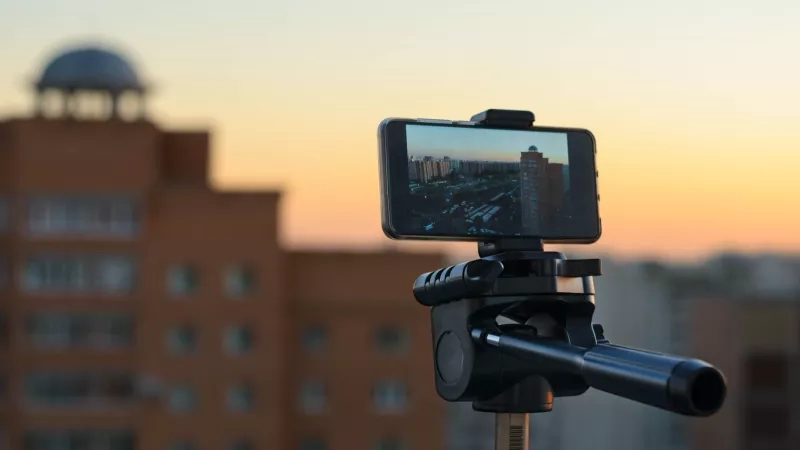 Mobile phone mounted on a tripod taking a picture of a cityscape at sunset.