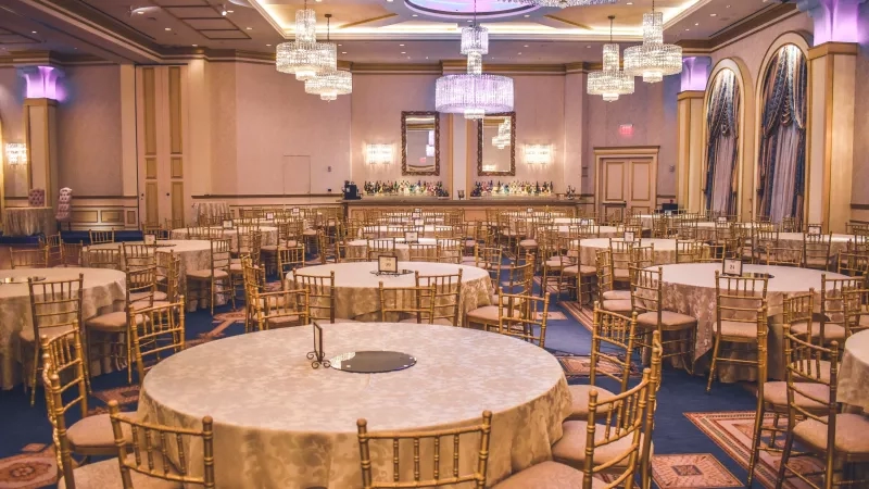 Gold chairs with white tablecloths in the middle of the room, chandeliers hanging from the ceiling.
