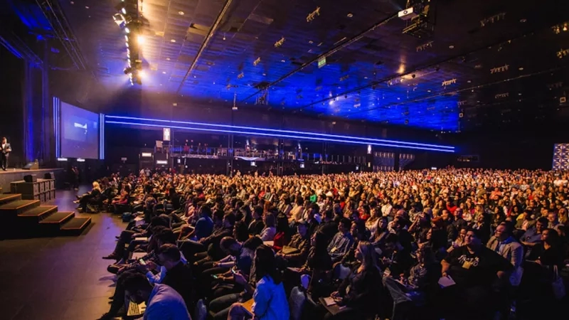 A conference room is filled with a large group of people sitting in rows of chairs.