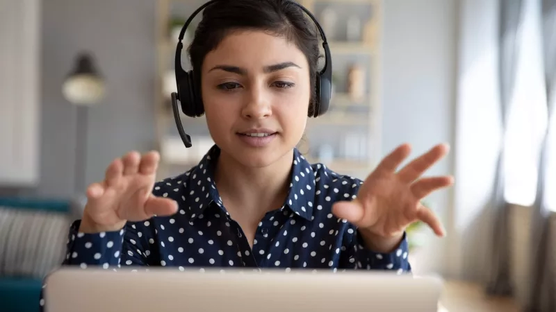 Woman wearing headphones, going through virtual training on a laptop in a room.