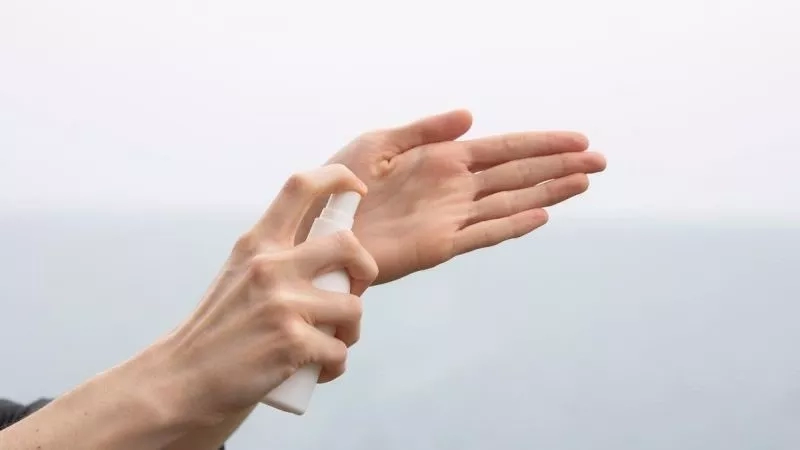 Person spraying their hands with sanitizer while holding it in their other hand.