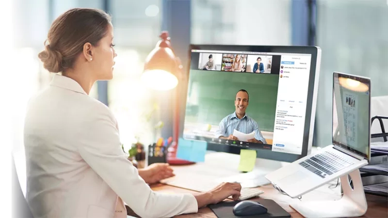 A woman is working on a computer while in a video call with others.