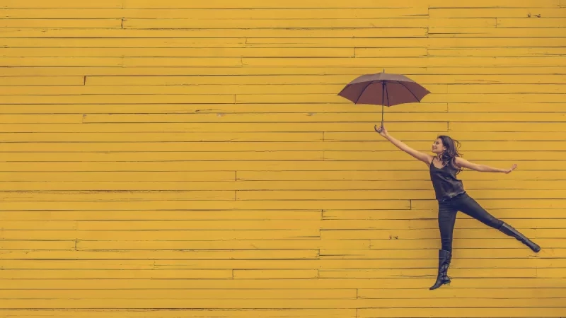 Woman jumping with an umbrella against a yellow wall, illustrating secrets to success in business.