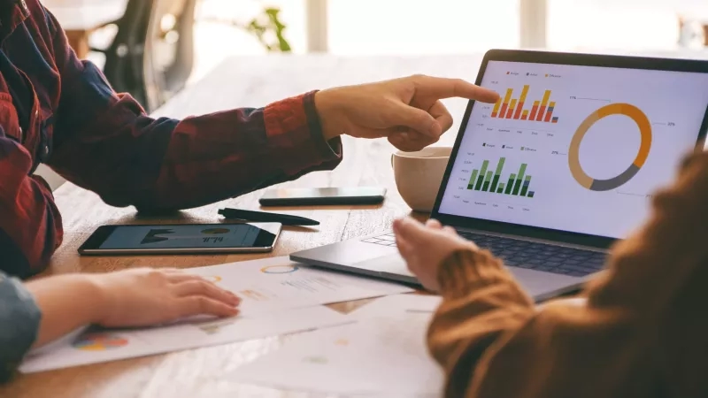 Three people looking at financial information on a laptop screen and a graph on a piece of paper.