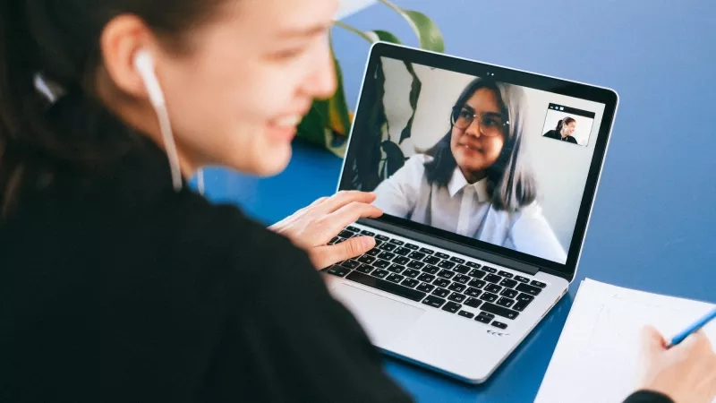 Woman on video call with another woman while writing on a piece of paper.