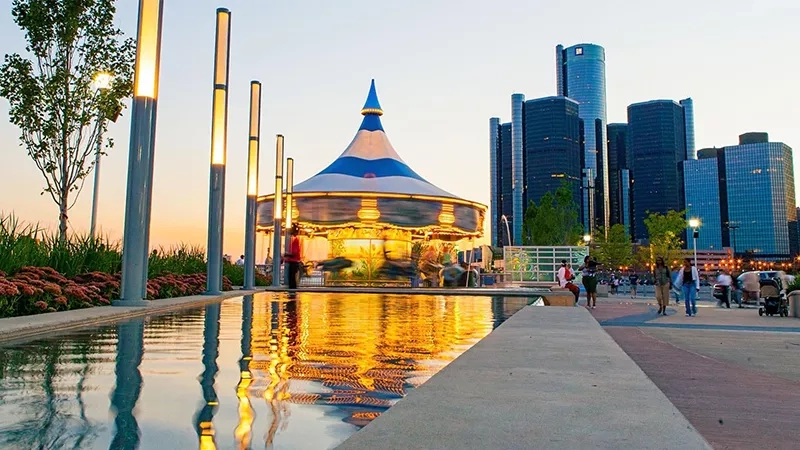 A carousel in downtown Detroit with a pool and people walking in the background.
