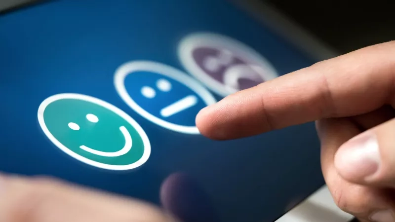 A hand is touching a screen that has a smiley, expressionless, and sad face on it.