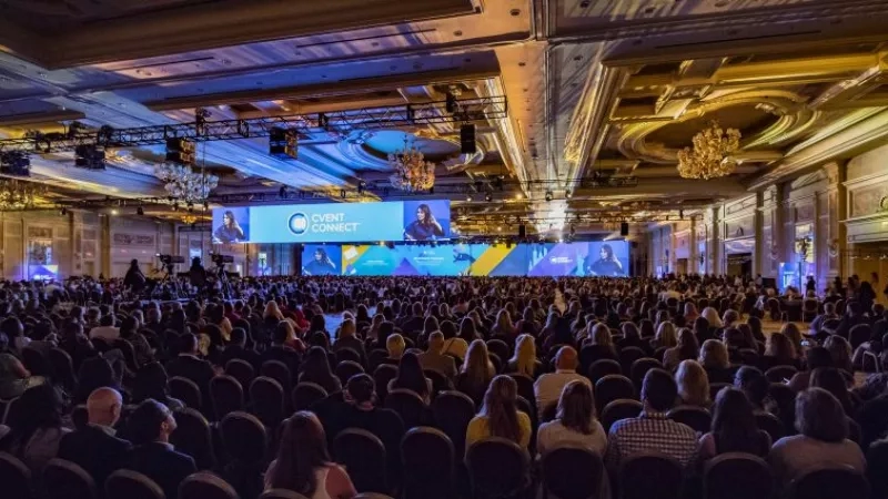 A large conference hall with people sitting in chairs and a stage with large screens at Cvent Connect.