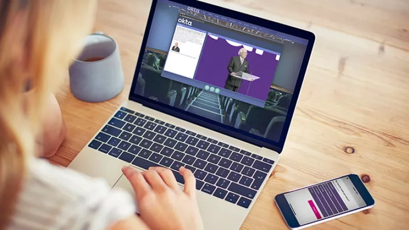 Woman using a laptop to view a virtual conference with a smartphone next to her on a table.