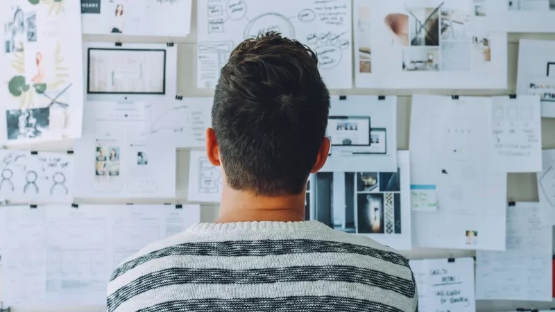 A man standing before a wall with a virtual event strategy execution plan pasted on it.