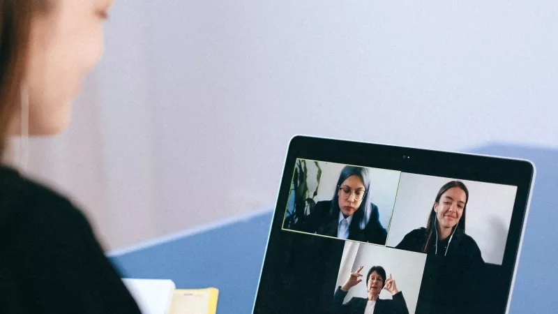 A woman is sitting at a desk and looking at a laptop with three people on it.