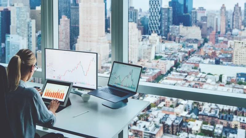 Woman looking at revenue graphs on computer with city view in background.