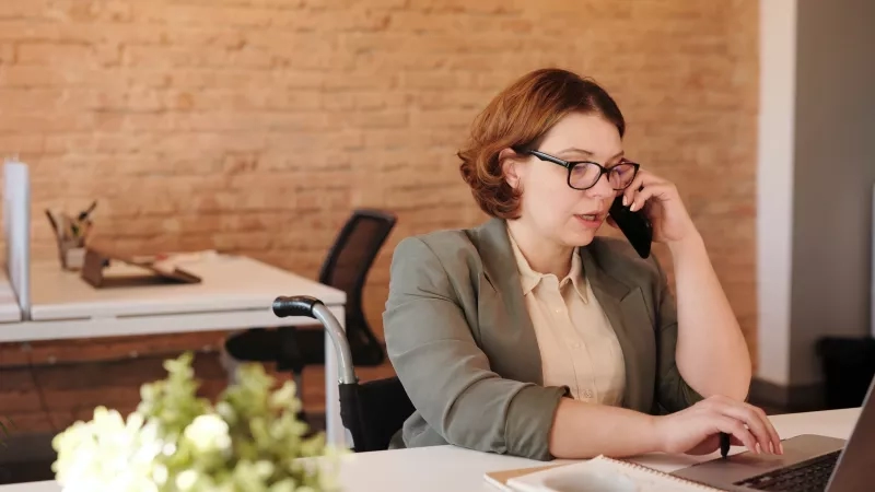 A woman in an office speaking on the phone while sitting at her desk in an office.