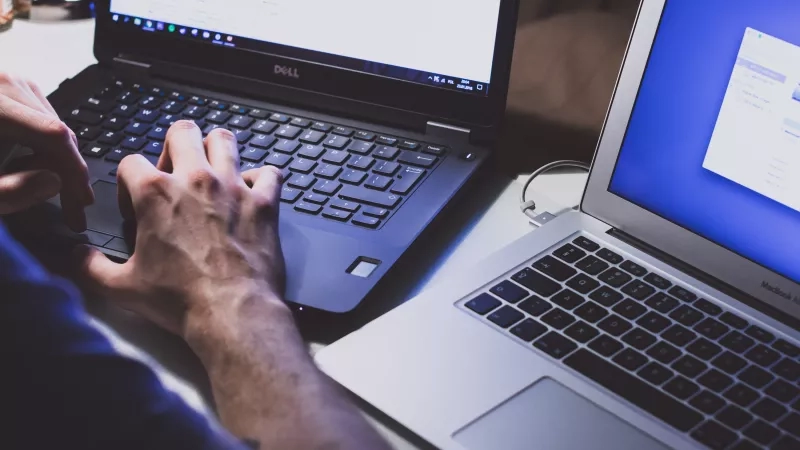 A person typing on a laptop with another laptop next to them on a desk.