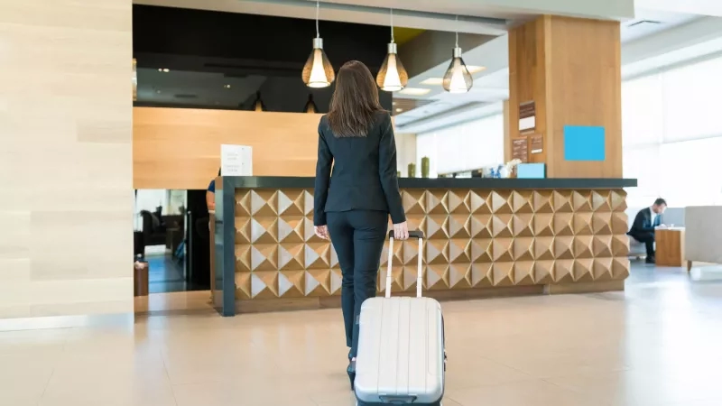 Woman with suitcase walking into hotel lobby and checking in at front desk.