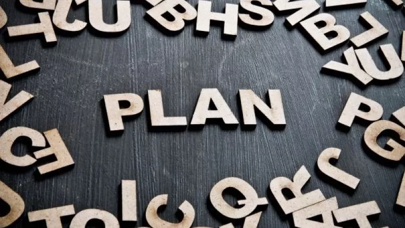 Wooden alphabet letters spell "plan" on a board, surrounded by other letters, for hybrid event planning.