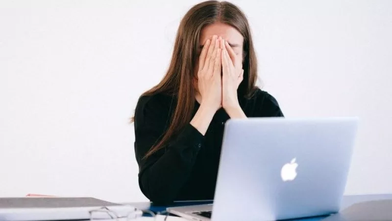 Woman looking stressed out while working on a laptop at her desk at work.