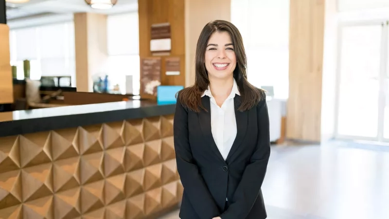 Hospitality management professional smiling in hotel lobby with wood and geometric design elements and bright ambiance.