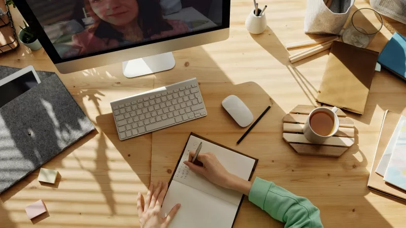 Person writing in a notebook during a virtual event on a computer.